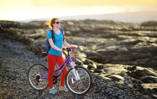 woman with red pants standing with her bike looking out over lava rock