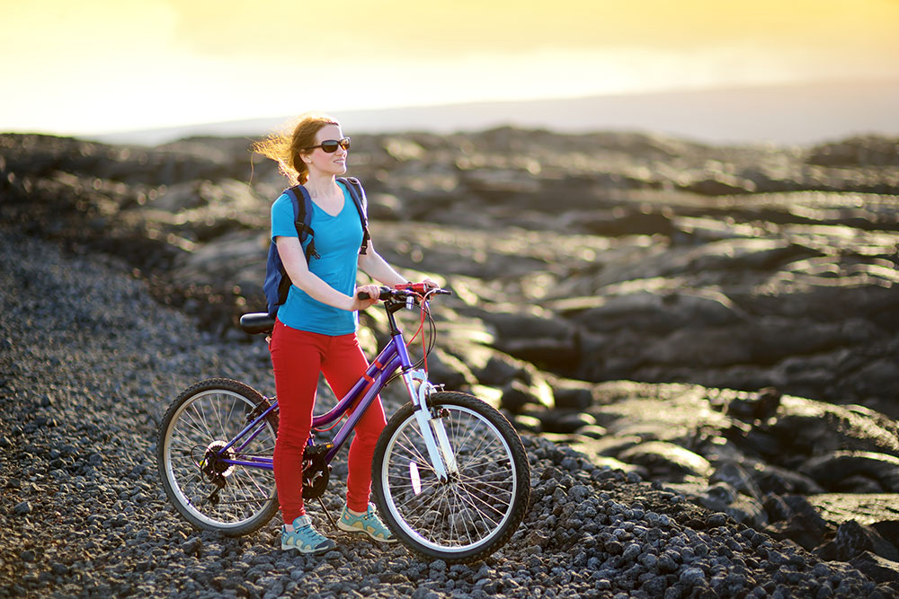 woman with red pants standing with her bike looking out over lava rock