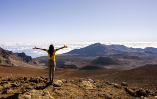 Woman standing on the summit of Haleakala Crater in Maui, watching the sunrise.