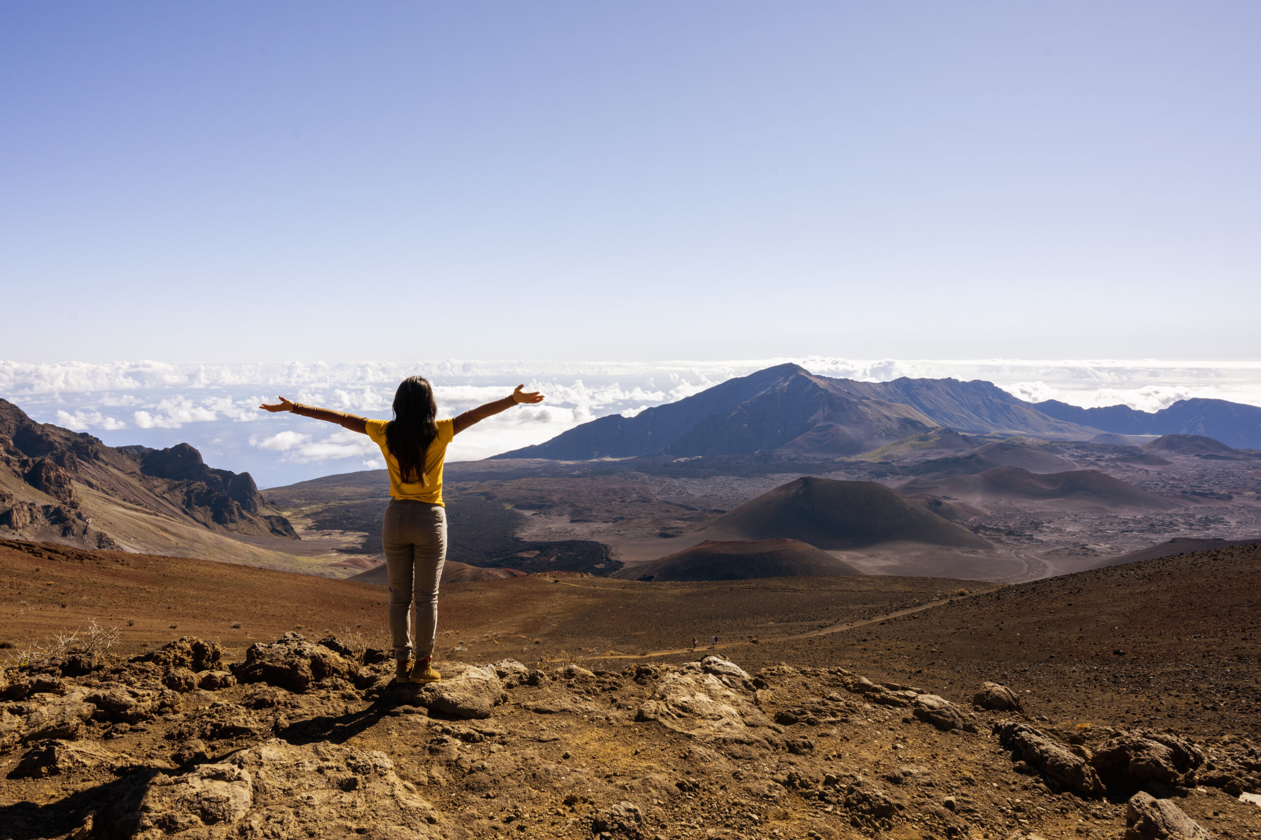 Woman standing on the summit of Haleakala Crater in Maui, watching the sunrise.