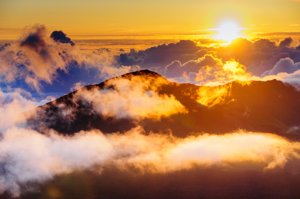 Sunrise over a mountain peak with clouds and bright orange hues.