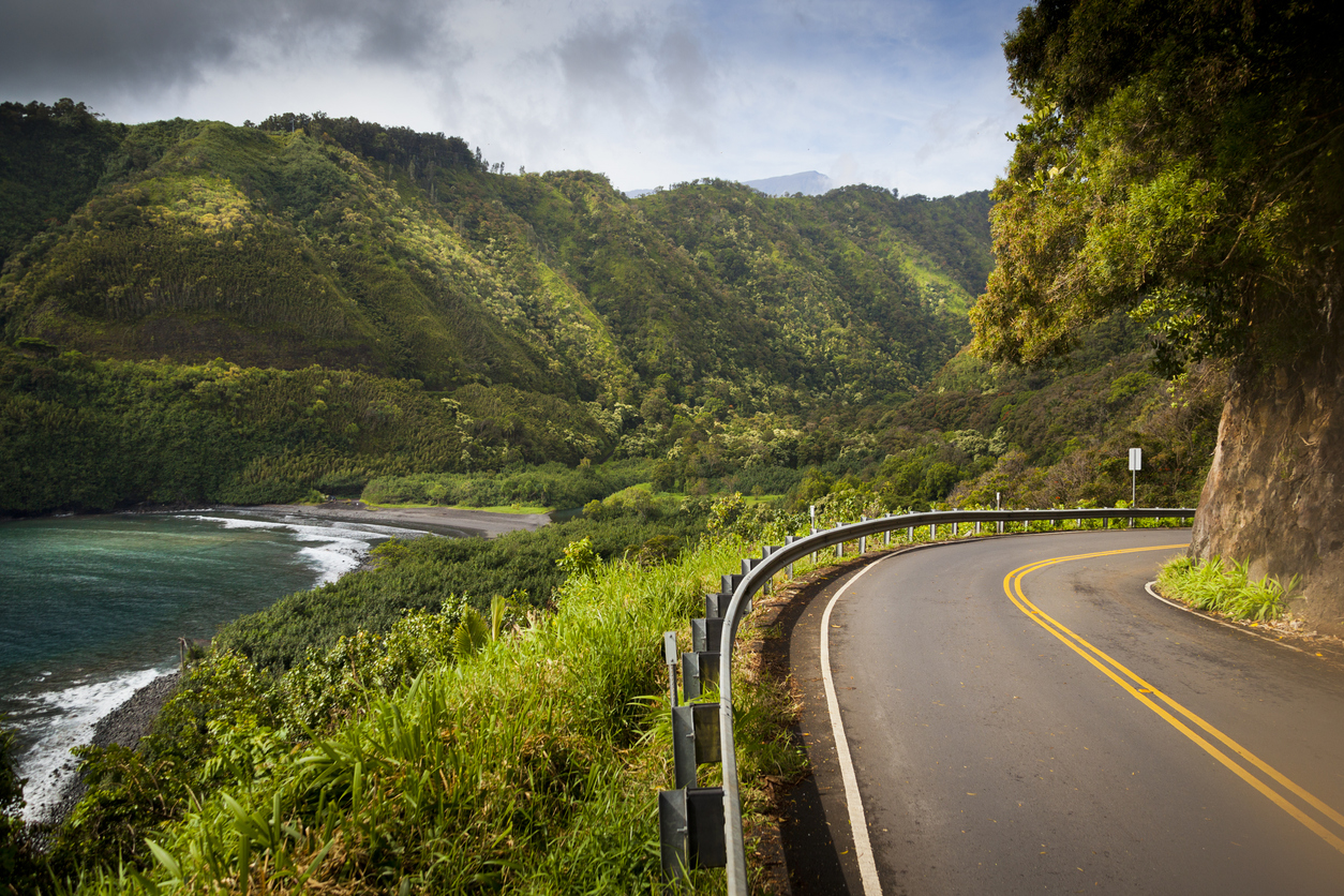 Curved coastal road with guardrails, lush green mountains, and ocean.