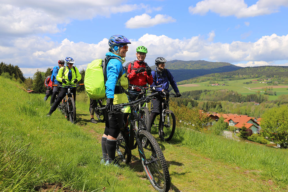 Group of cyclists on a scenic hillside trail with lush countryside view.