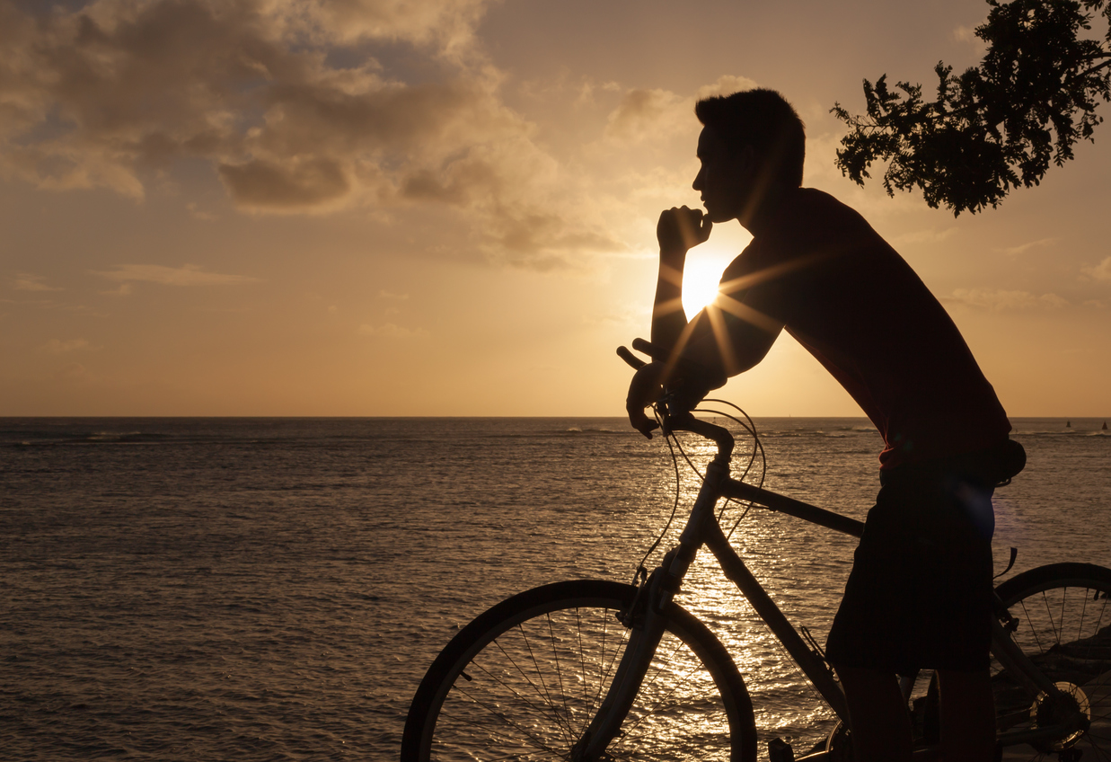 Silhouette of a person on a bicycle by the shore at sunset.