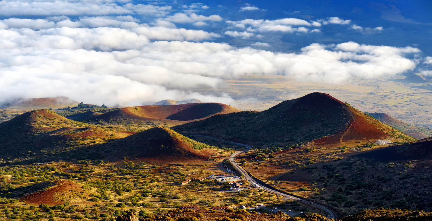 Curved road through lush, hilly landscape under a cloudy sky.
