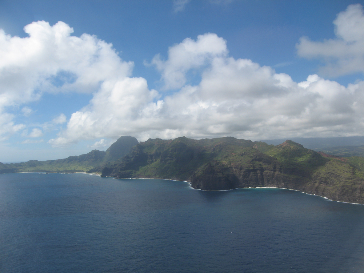 Aerial view of a coastal mountain range with blue ocean and cloudy sky.