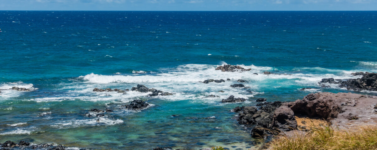 Rocky ocean shoreline with waves and blue sky.