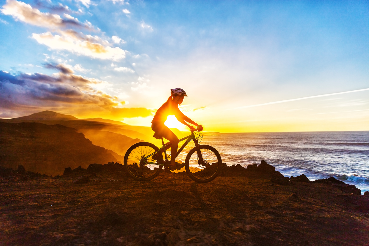 Silhouette of cyclist on rocky coast at sunset.