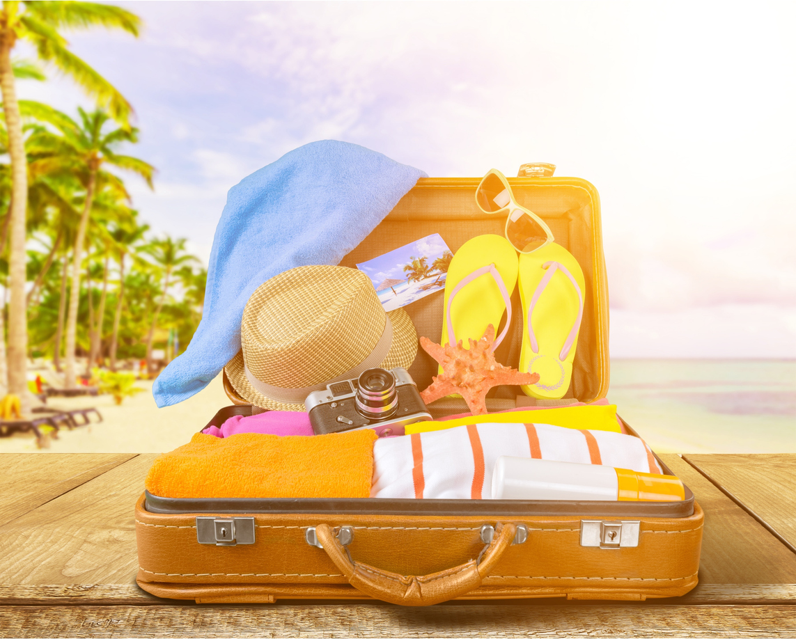 Open suitcase with beach items on a tropical beach background.