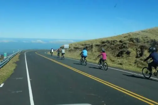 Cyclists ride on a rural road with clear skies and open landscape.