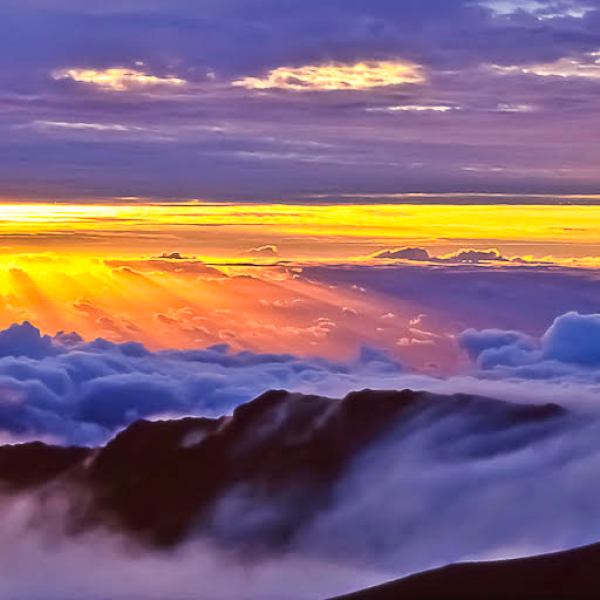 Sunrise over mountains with clouds and sun rays illuminating the sky.